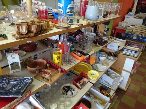Tässä Harrin ottamassa kuvassa esitellään Vaahtera-kirppiksen tavaravalikoimaa. Valokuva pöydästä, jossa monta tasoa ja jotka täynnä erilaisia lautasia, kippoja, astioita ja koriste-esineitä.