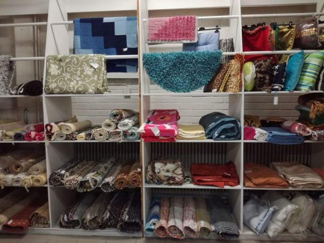 Valokuva valkoisesta hyllyköstä, jossa lokerot täynnä erilaisia kankaita ja tyynyjä.