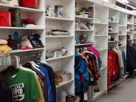 Korkea hyllykkö, jossa runsaasti erilaisia värikkäitä vaatteita ja astioita.