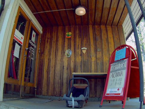 V%C3%A4rikuva+otettu+kalansilm%C3%A4objektiivilla.+Värikuva otettu kalansilmäobjektiivilla. Kuvassa näkyy puuseinää ja -kattoa, oikealla punainen kyltti, jossa aukioloajat, ja keskellä lapsen turvaistuin.