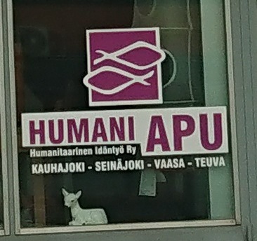 Valokuva ikkunateippauksesta, jossa lukee: Humani Apu. Humanitaarinen Idäntyö Ry. Kauhajoki, Seinäjoki, Vaasa, Teuva.