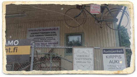 Valokuva valkoisesta puuseinästä, ja katossa roikkuvasta vanhasta polkupyörästä.