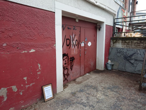 Värivalokuva Voikoin julkisivusta. Punavalkoinen seinä, johon spray-maalattu VoiKoi mustalla ja sen alle pelkistetty ihmishahmo.