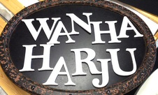 Wanhan Harjun mainoskyltti, jossa mustaa ovaalia taustaa vasten valkoisin kirjaimin sanat Wanha Harju.