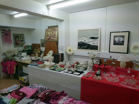 Kuvassa Alajärven Kellarikirppiksen tavarapaljoutta. Pöydät täynnä kaikenlaisia pienesineitä, seinillä tauluja ja muita tavaroita.