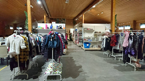 Valokuva hallista, jossa puukatto ja avara käytävä, jonka varrella erilaista kirppistavaraa, kuten vaatteita.