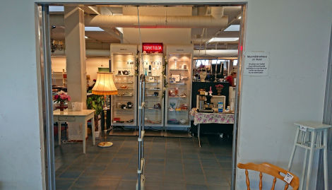 Värivalokuva ovensuusta, jonkak eskellä on porttihälytin ja takana näkyy lattialamppu, jossa valo päällä, sekä valaistuja vitriinejä.