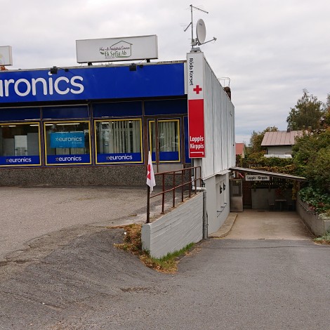 Värivalokuva kiinteistön julkisivusta. Taivas on pilvinen. Vasemmalla Euronicsin sininen julkisivu, sen vieressä luiska, joka vie alaspäin.
