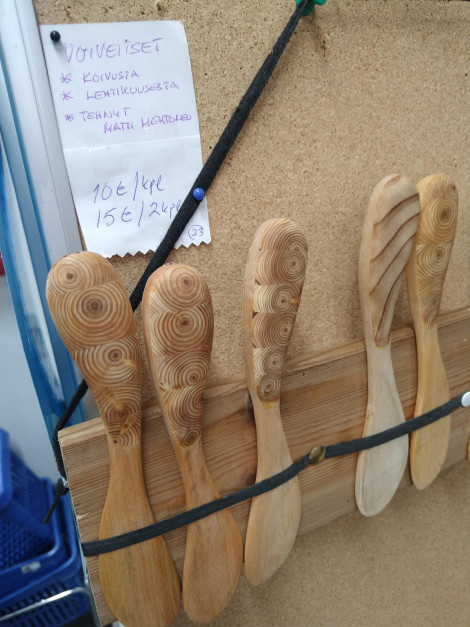 Värivalokuva puisista voiveitsistä, jotka aseteltu nyöriin pystyasentoon. Niiden yläpuolella valkoinen lappu, jossa kerrotaan voiveisten olevan koivusta, lehtikuusesta, ym.