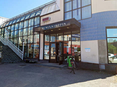 Aurinkoisena kesäpäivänä otettu värivalokuva monikerroksisesta, modernilta näyttävästä rakennuksesta, jossa Remixkirppiksen logo ovenkäynnin yläpuolella.