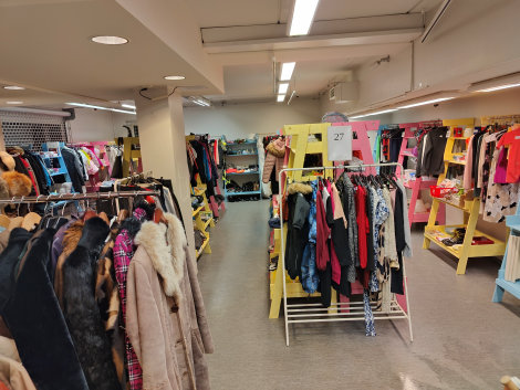 Värivalokuva liiketilasta, jossa värikkäitä vaatteita rekeissä ja hyllyissä eri puolilla.