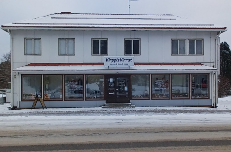Värivalokuva kaksikerroksisesta rakennuksesta, jossa ykköskerroksessa suuret lasi-ikkunat ja kiinteistön keskellä seinässä mainoskyltti, jossa lukee: "Kirppis Virrat".