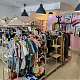 Värivalokuva, jossa näkyy myyntirekkejä täynnä erilaisia vaatteita ja asusteita. Taustalla on sovituskoppi.
