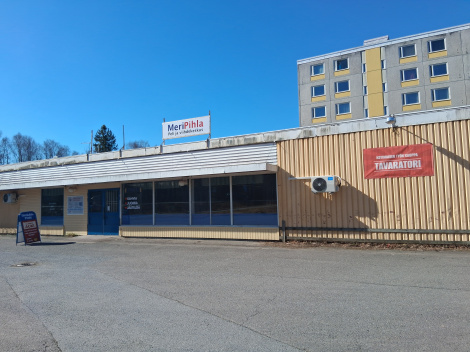 Kuvassa Tavaratorin julkisivu. Kuvasta kiitos Reijolle. Aurinkoisena kesäpäivänä otettu värivalokuva MeriPihla-rakennuksesta, jonka julkisivun oikeassa reunassa on Tavaratorin punainen mainoslakana.