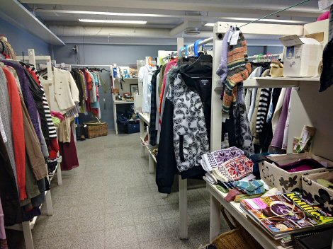 Kuvassa esimerkkejä Hiiden Kirppiksen tavaravalikoimasta. Vaatteita ja muita tavaroita Hiiden Kirppiksen valkoisissa pöydissä.