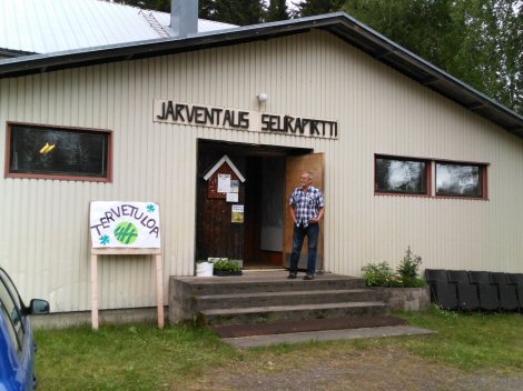 Järventaus Seurapirtin julkisivu, jossa tervetuloakyltti vasemmalla ja ovensuu auki.